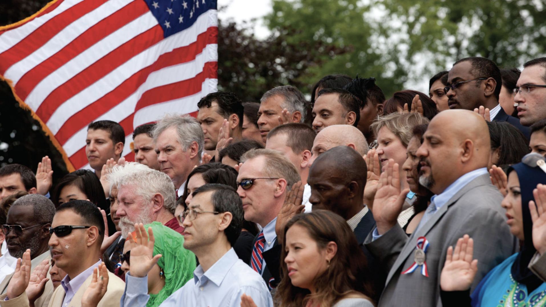 lots of people holding right hand up next to American flag