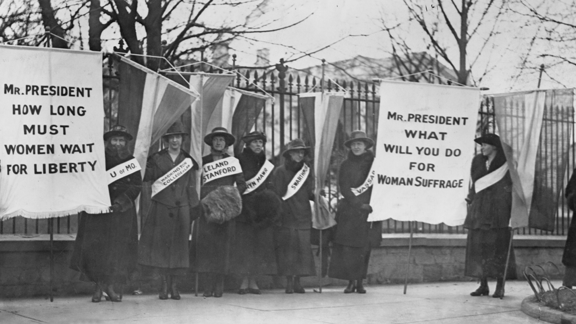 Woman standing in front of fence holding banners