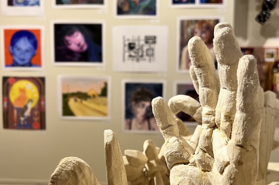 sculpture of hands in the foreground with paintings on the wall in the background