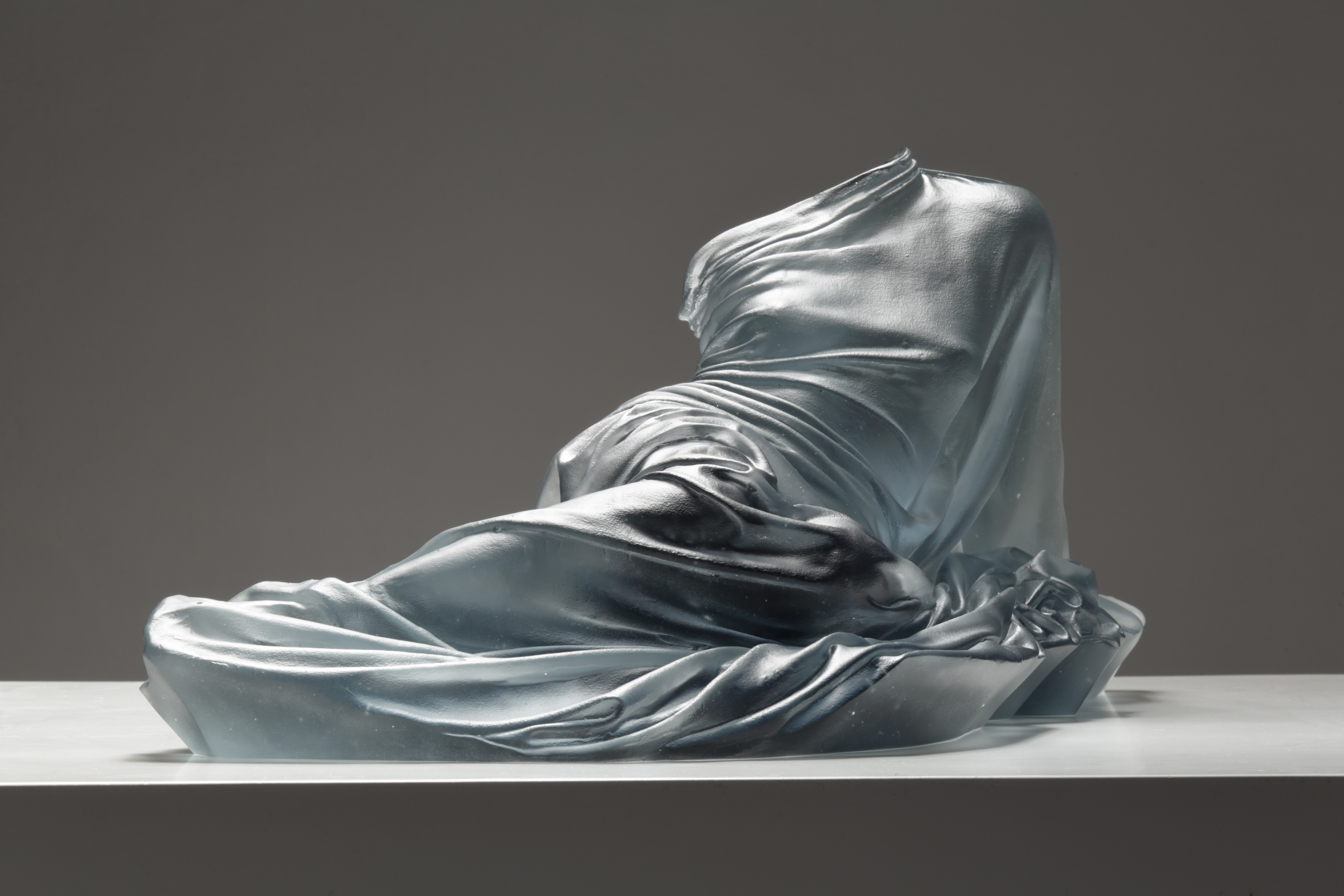 Form of woman laying, just glass dress providing form