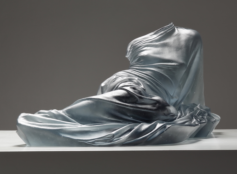 Form of woman laying, just glass dress providing form