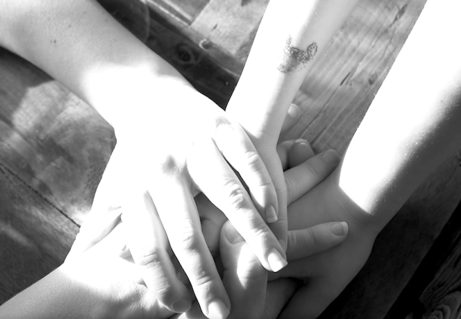 close up three hands piling on top of each others hands black and white image still from video